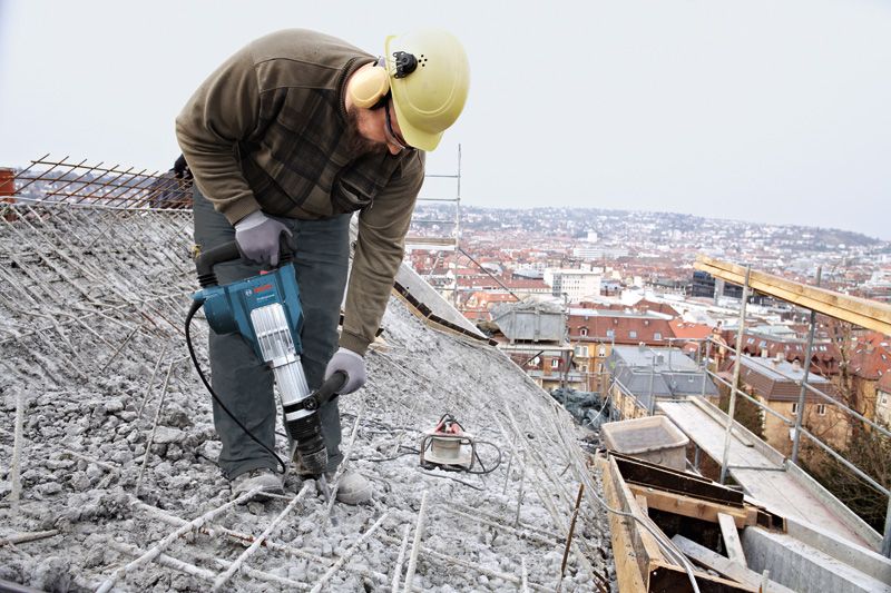 一名佩戴安全设备的人员使用破碎锤破碎屋顶上的混凝土。.