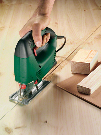 一名工人引导拼图锯沿着标记线切割胶合板。.