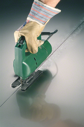 佩戴安全设备的人使用曲线锯在金属上切割出一条直线。.