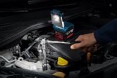 一名工人用扳手修理汽车发动机，旁边还有无绳工作灯。.