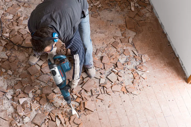 一名佩戴安全设备的人员使用破碎锤砸碎地砖。.
