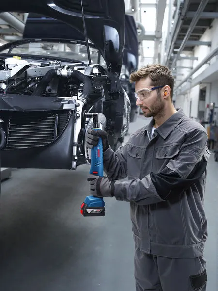 一名佩戴安全设备的人员使用无绳电动工具拧紧车架上的螺栓。.