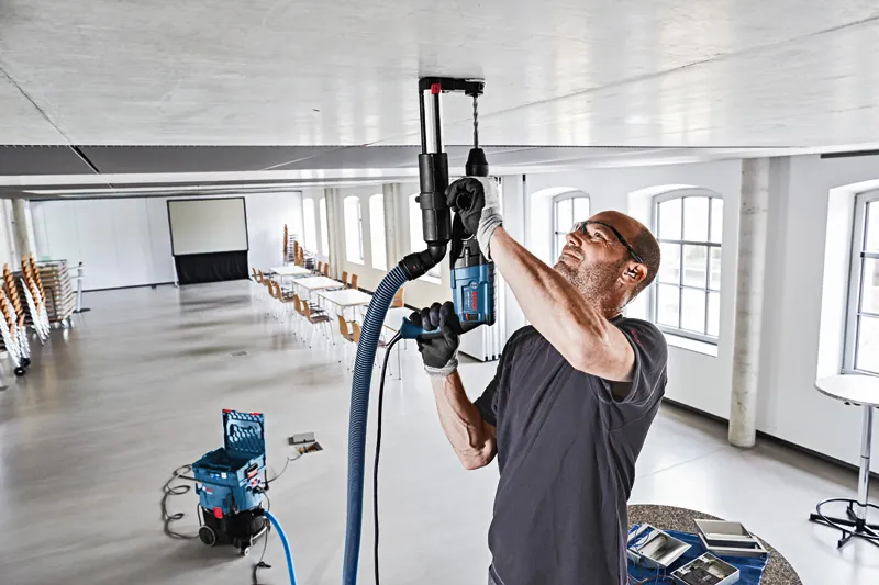 一名佩戴安全设备的人员正在用除尘系统钻入天花板。.