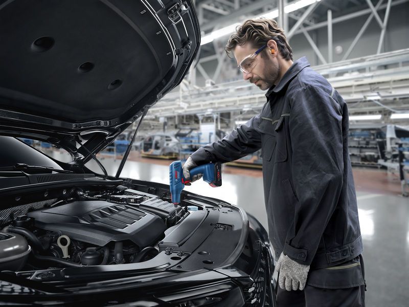 一名佩戴安全设备的人员在汽车装配线上使用热风枪。.