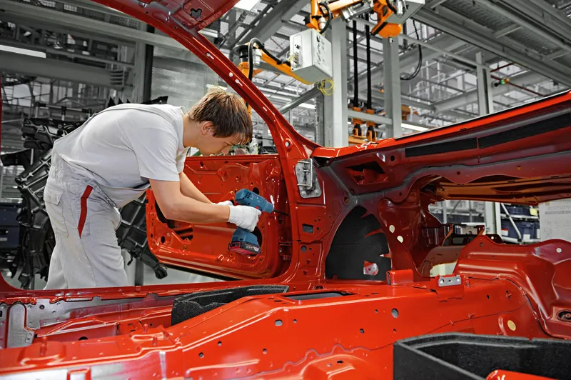 一名佩戴安全设备的人员在工厂里使用无绳电钻组装车门。.