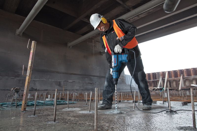 建筑工地上，一名佩戴安全设备的工人正在用旋转锤钻入混凝土。.