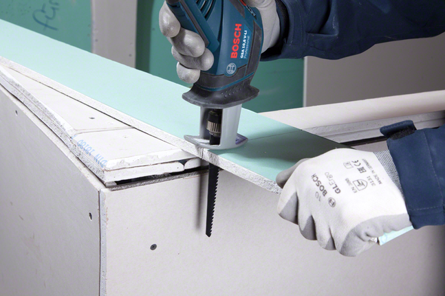 一名佩戴安全设备的工人正在用往复锯切割干墙。.