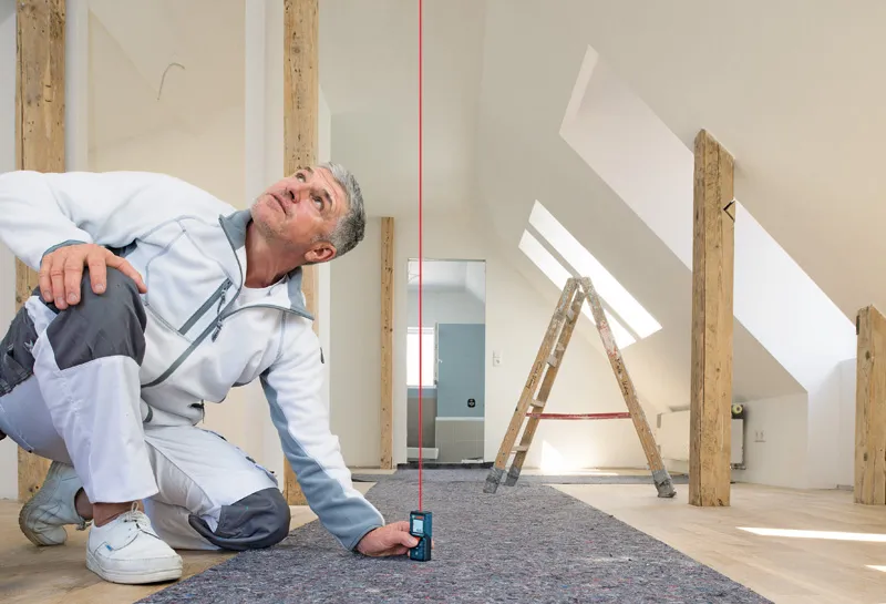 一名男子使用激光测量仪检查明亮阁楼房间内的垂直对齐情况。