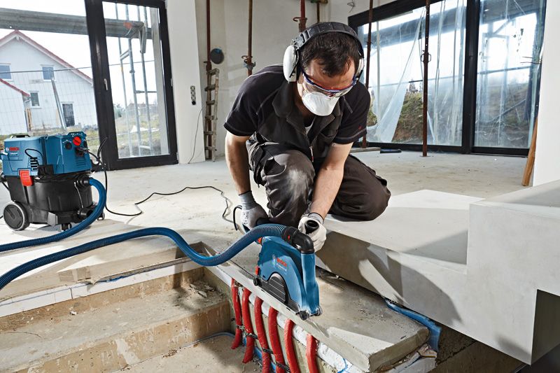 一名佩戴安全装备的人员使用墙体开槽机切割裸露管道附近的混凝土。