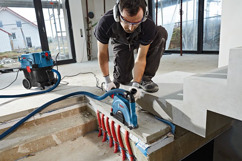 一名佩戴安全设备的人员使用墙面开槽机在裸露管道上方的混凝土上进行开槽。.