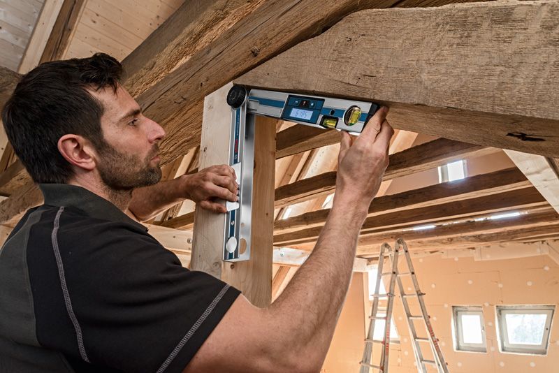 人们在木屋顶下用数字测斜仪检查木梁的角度。.