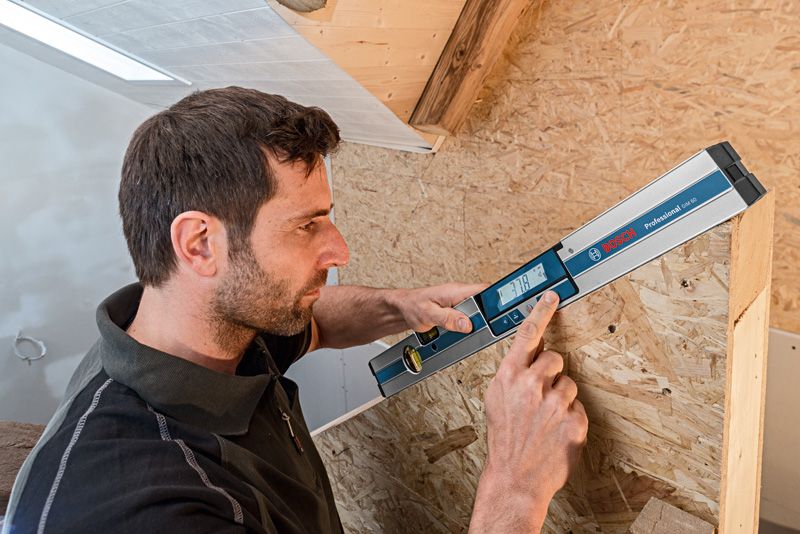 一个人使用数字测斜仪测量木结构的角度。.