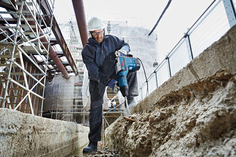 一名佩戴安全设备的人员在建筑工地上使用旋转锤破碎混凝土。.