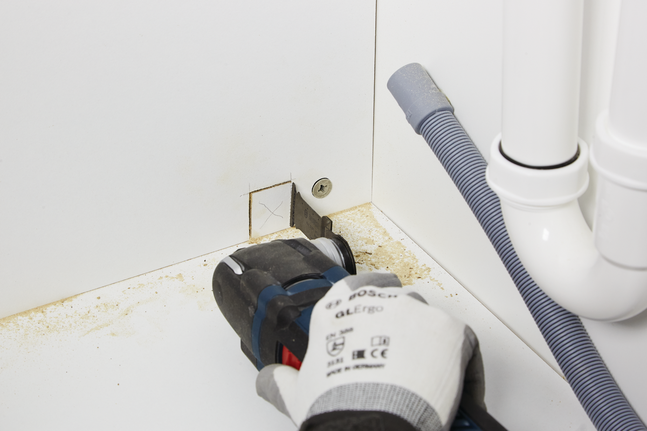 工人佩戴安全设备，用电动工具在柜子上切出一个方形开口。.