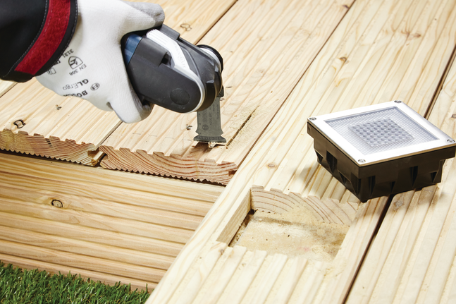 工人佩戴安全设备，使用多功能工具在木质甲板上切割出凹槽。.