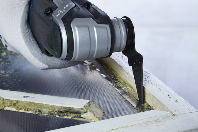 戴着手套的手使用振荡工具切割旧窗框油灰。.