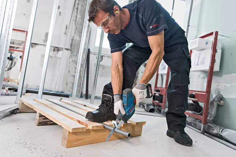 一名佩戴安全设备的人员使用往复锯切割金属管道。.