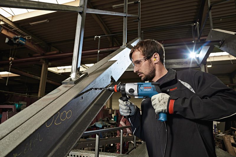 一名佩戴安全设备的人员使用钻头在金属梁上钻孔。.