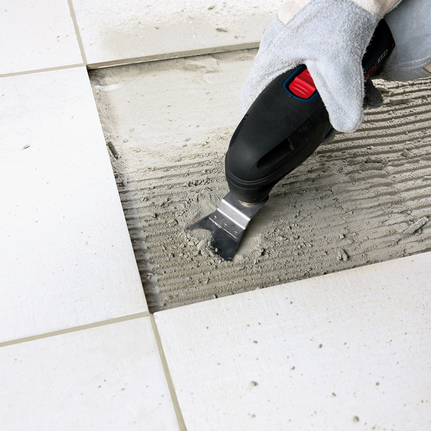 工人佩戴安全设备，使用多功能工具去除地砖之间的粘合剂。.