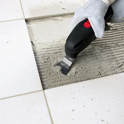 工人佩戴安全设备，使用多功能工具去除地砖之间的粘合剂。.