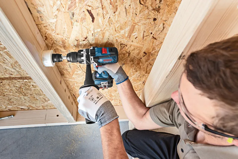 一名佩戴安全设备的人员正在用孔锯在木板上钻孔。.