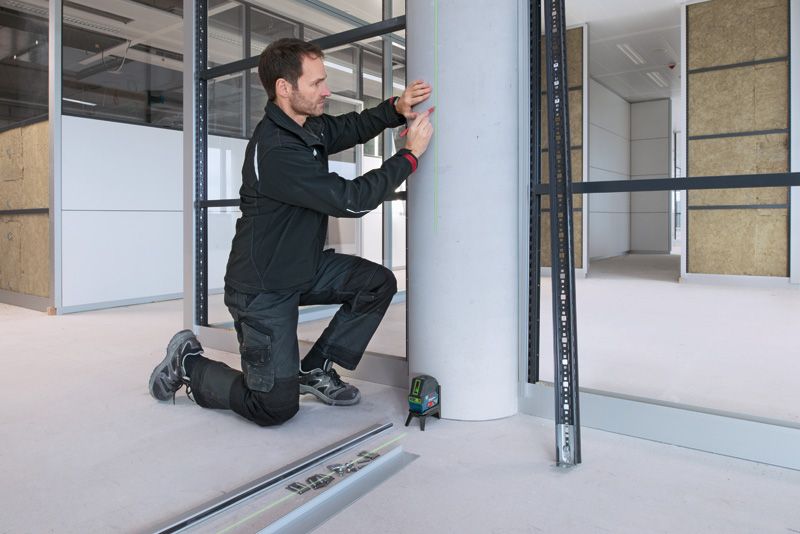 一名佩戴安全设备的人员正在使用激光调平工具标记混凝土柱。.