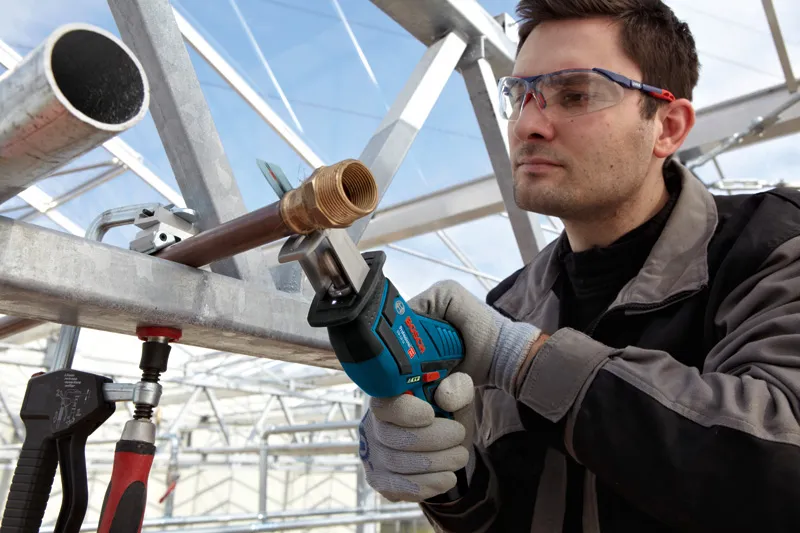 一名佩戴安全装备的人员正在用往复锯切割金属管。