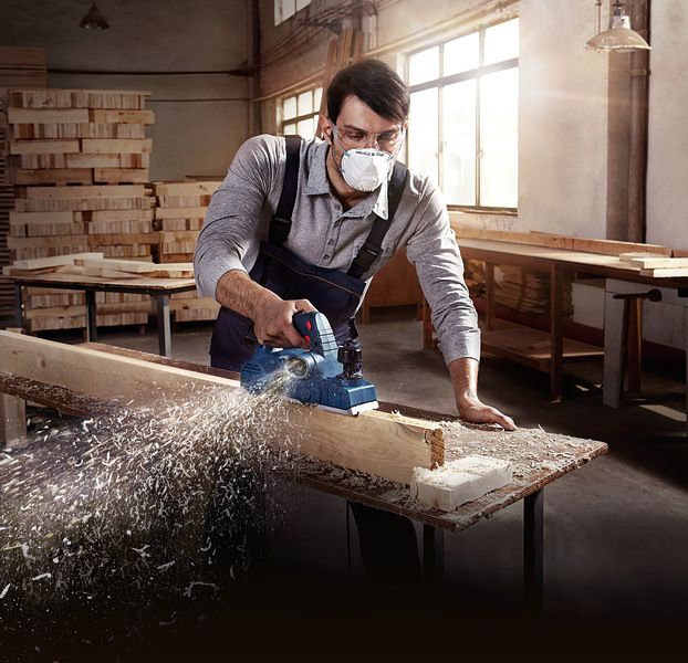 一名佩戴安全设备的工人在车间刨木梁。