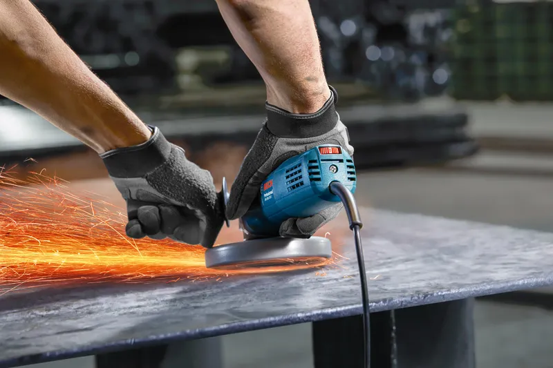 一名佩戴安全设备的人用角磨机研磨金属，产生火花。.