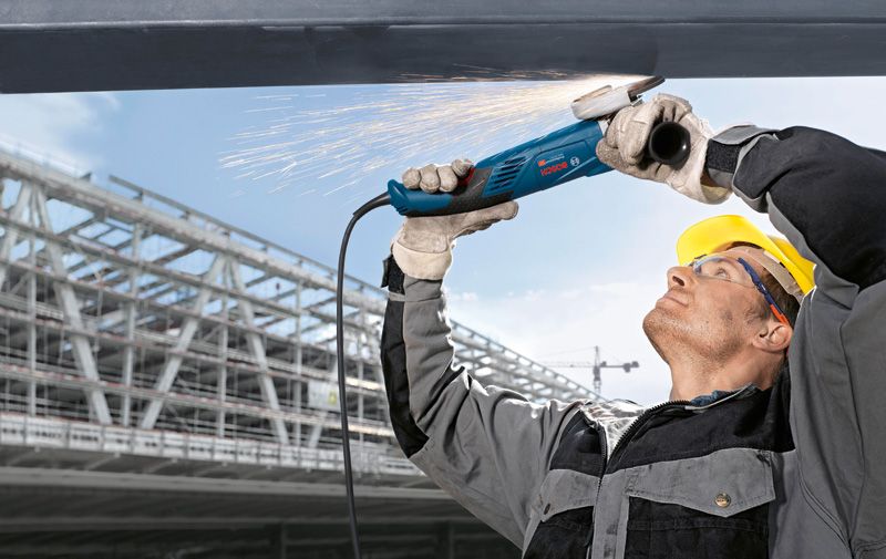 一名佩戴安全设备的人在头顶上研磨金属，产生火花。.