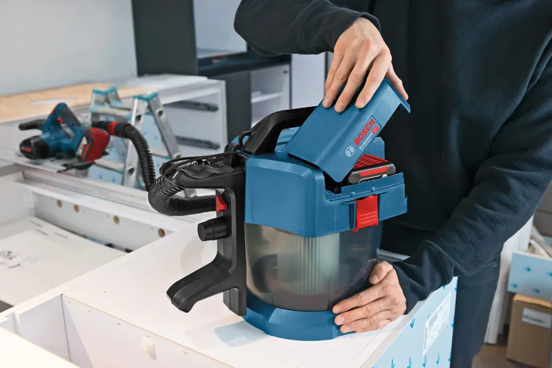 一个人将电池插入工作台上的无绳除尘器中。.