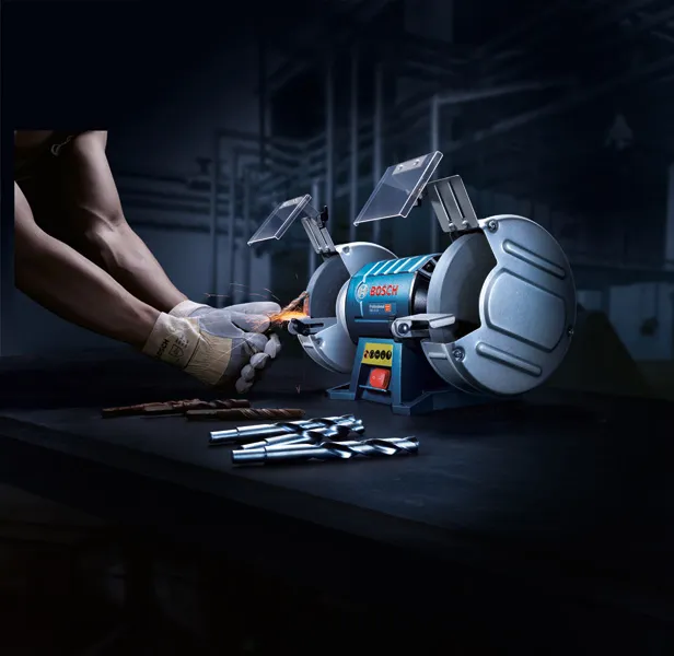 一名佩戴安全设备的人正在用双轮台式砂轮机磨钻头。