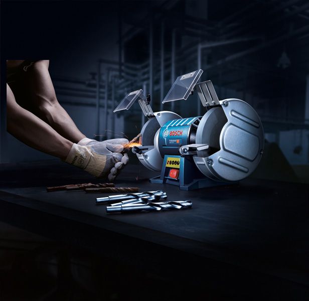 一名佩戴安全设备的人正在用双轮台式砂轮机磨钻头。