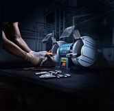 一名佩戴安全设备的人正在用双轮台式砂轮机磨钻头。