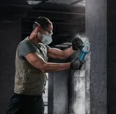 一名佩戴安全设备的人员正在用角磨机打磨混凝土墙。.