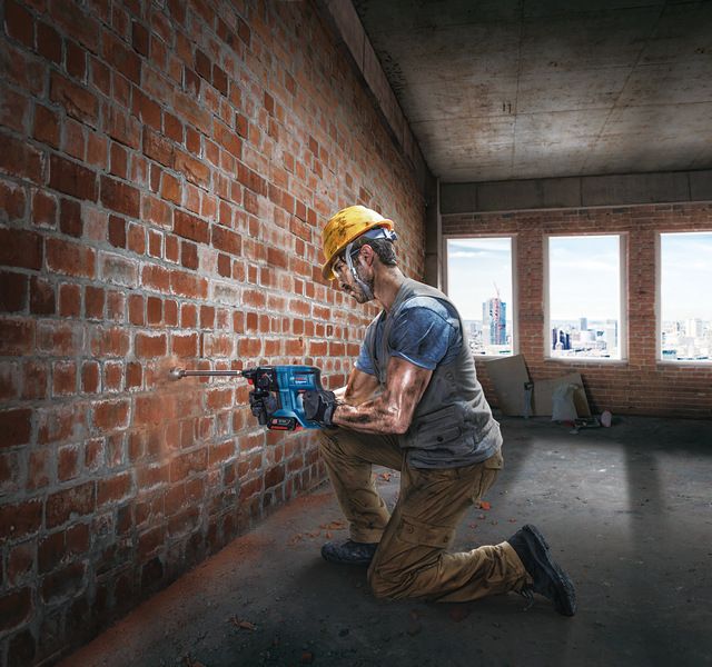 一名佩戴安全设备的人员正在向正在建造的建筑物内的砖墙上钻孔。.