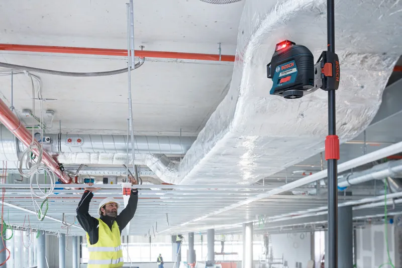 一名佩戴安全设备的人员使用激光调平工具对准天花板框架。.