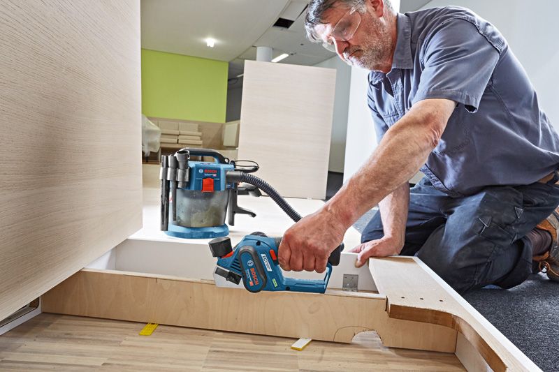 一名佩戴安全设备的人员使用无绳刨床打磨木板。.