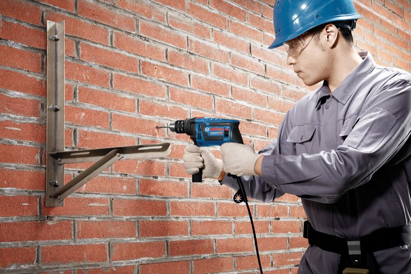 一名佩戴安全设备的人员在砖墙上钻孔以安装金属支架。.