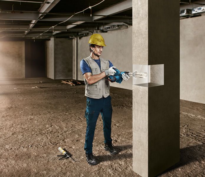 一名佩戴安全装备的人员正在建筑工地钻探混凝土柱。