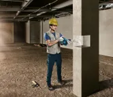 一名佩戴安全装备的人员正在建筑工地钻探混凝土柱。