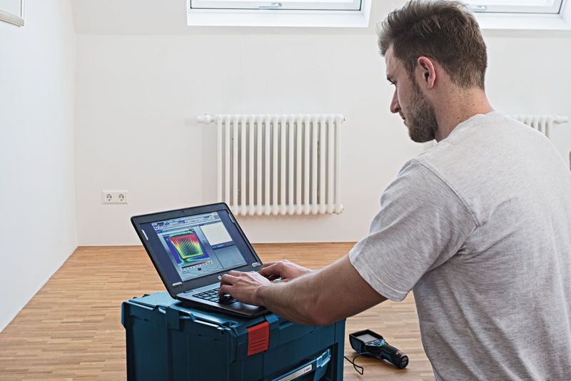 一名人员在装有散热器的房间里用笔记本电脑分析热像仪数据。.