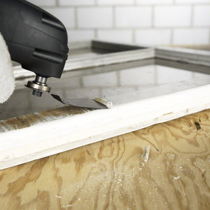 一名佩戴安全装备的人员使用多功能工具从窗框上移除材料。