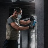 一名佩戴安全设备的人员使用角磨机打磨混凝土墙。.