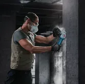 一名佩戴安全设备的人员使用角磨机打磨混凝土墙。.