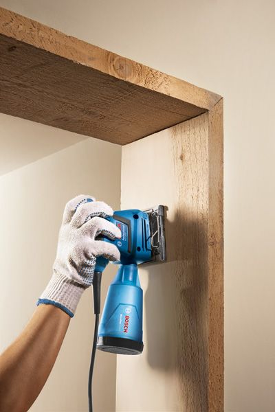 一名佩戴安全设备的人员正在使用电动工具打磨木门框。.