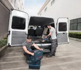 一辆敞篷货车旁的两名工人整理工具并使用无绳吸尘器。.