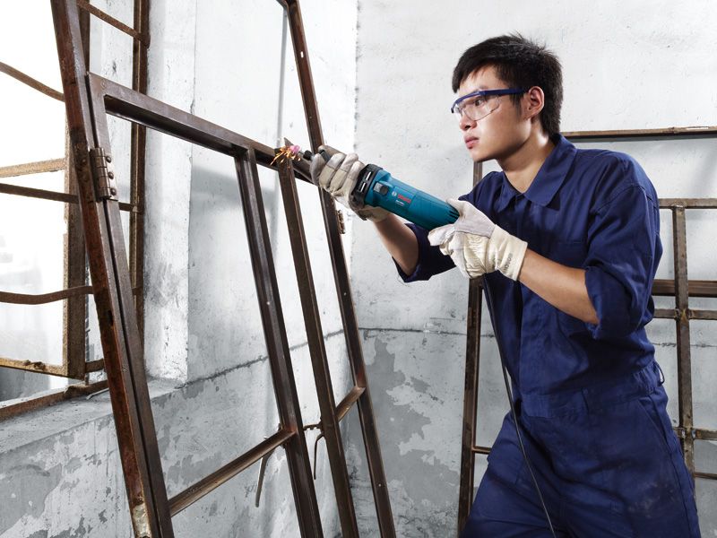 佩戴安全设备的人员使用直磨机打磨金属窗框。