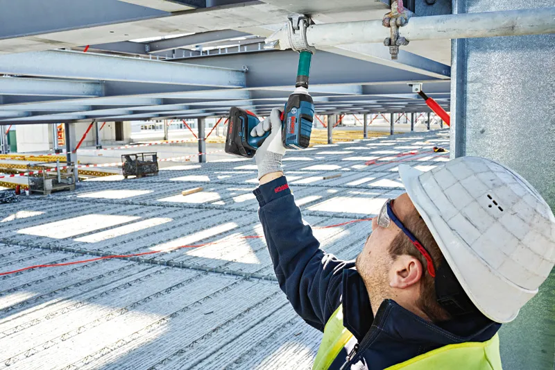 一名佩戴安全设备的人员使用无绳冲击扳手拧动金属梁。.