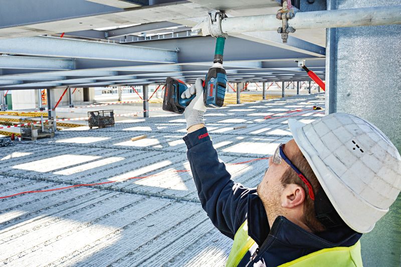 一名佩戴安全设备的人员使用无绳冲击扳手拧动金属梁。.